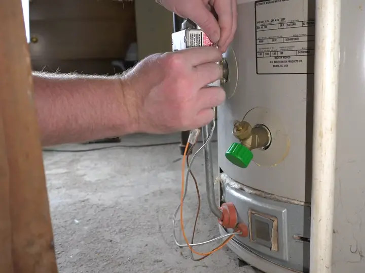 Technician checking the gas control valve on a tank water heater in a Revere basement